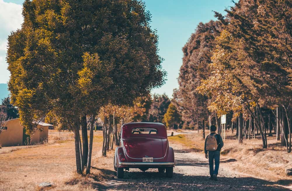 chico de espaldas y al lado un coche rojo vintage